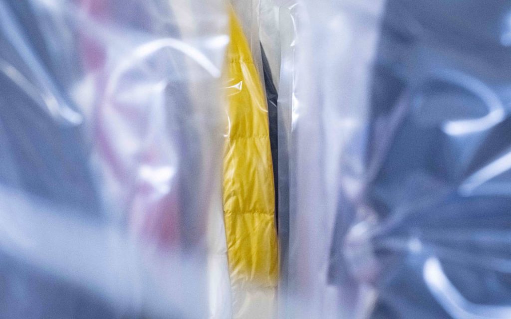 Clothing packaged in polythene layflat tubing. A yellow garment can be seen in focus, through a narrow slit of plastic packaging, which is out of focus