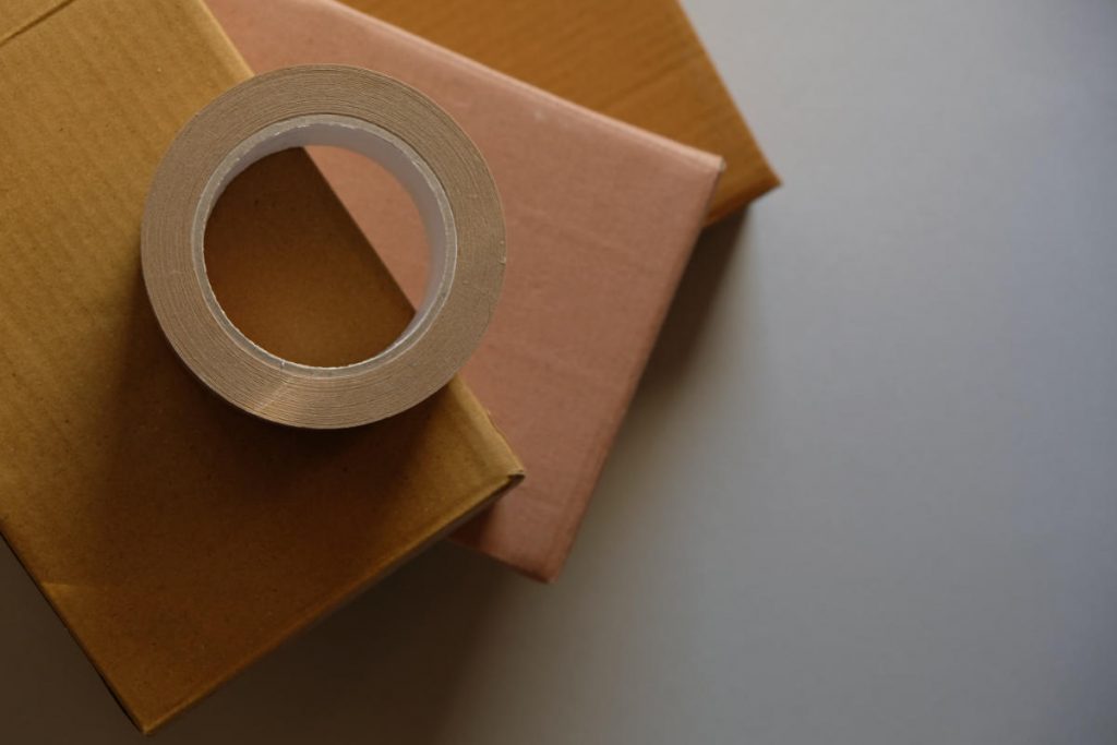 Packaging materials flat-lay. A roll of brown tape is placed on some boxes, stacked and arranged in a fan shape.