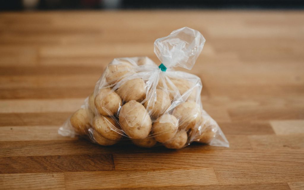 New potatoes in a clear polythene bag, with a green tape seal at the top, placed on a butcher's block.