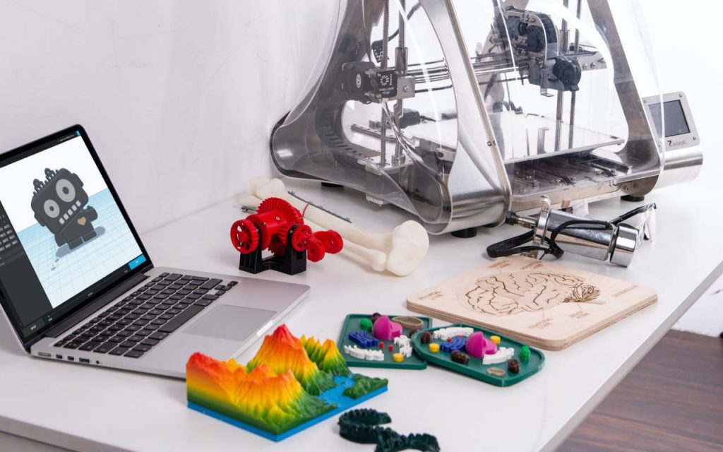 3d printing machine, printed plastic items and laptop on a white desk