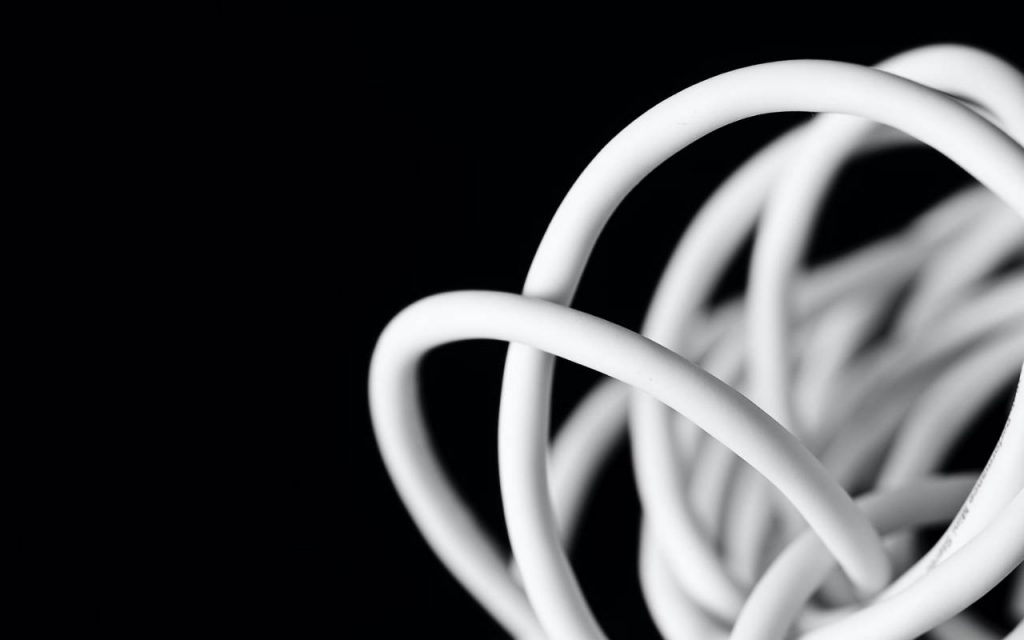A close up shot of a ball of white, plastic-coated cable on a black background