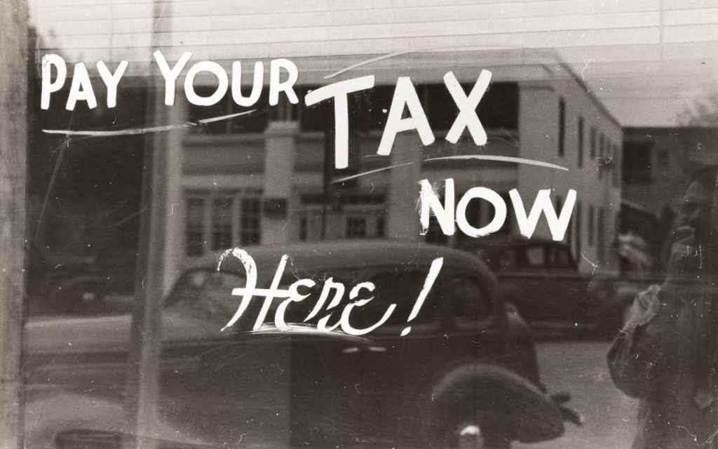 Very old black and white photo of Pay Your Tax HERE NOW sign on a window