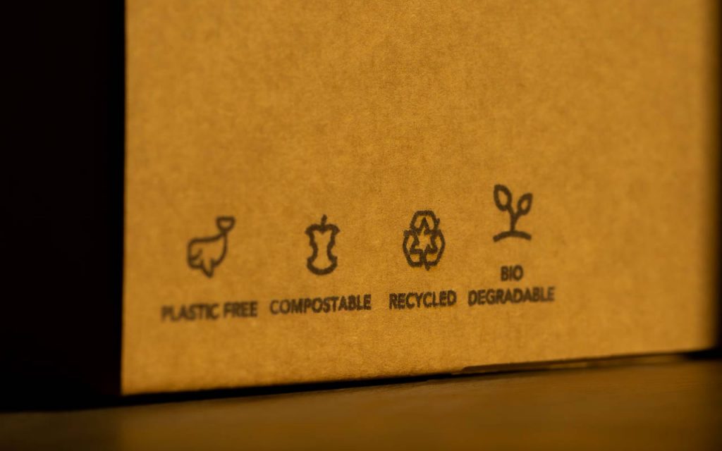 closeup photo of a raw cardboard box, printed with plastic free, bidegradeable, recycled and compostable symbols.