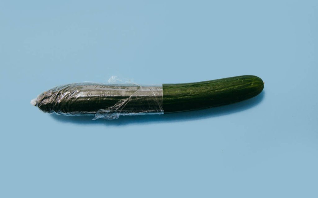 A cucumber partially wrapped in polythene film. Photographed on a pale blue background as a flat lay image