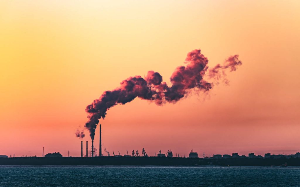 Factory or refinery on the water, pumping gases into the air at sunset