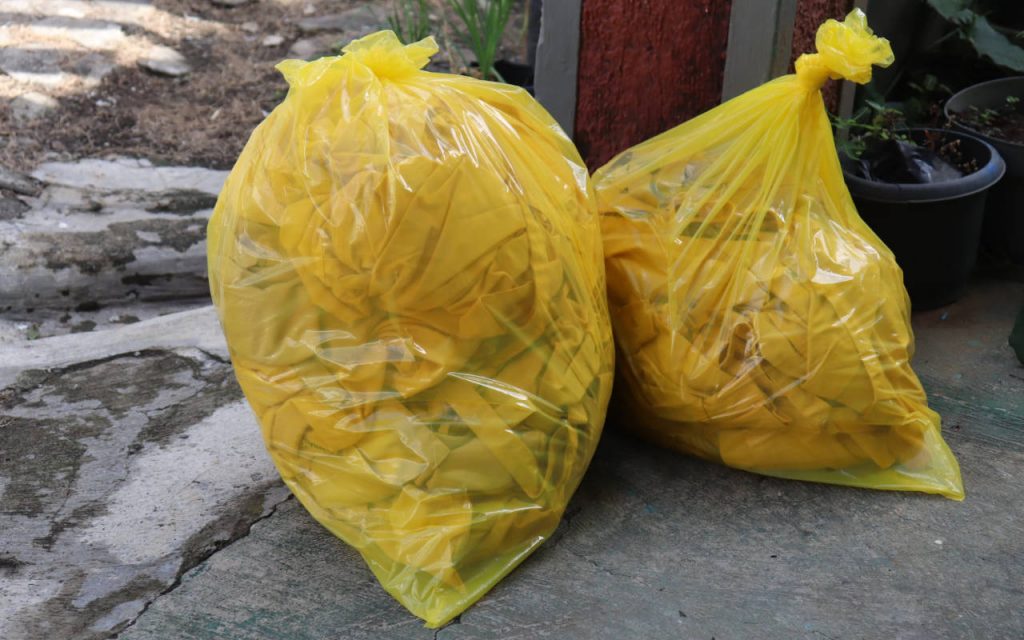 Two yellow hazardous waste bags – filled and deposited on conrete floor outside, during collection