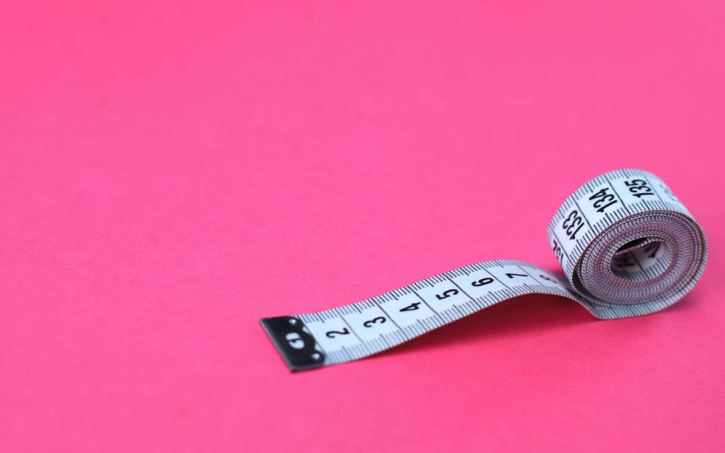 Close up photo of a white measuring tape, partially rolled up, on a vivid pink background.
