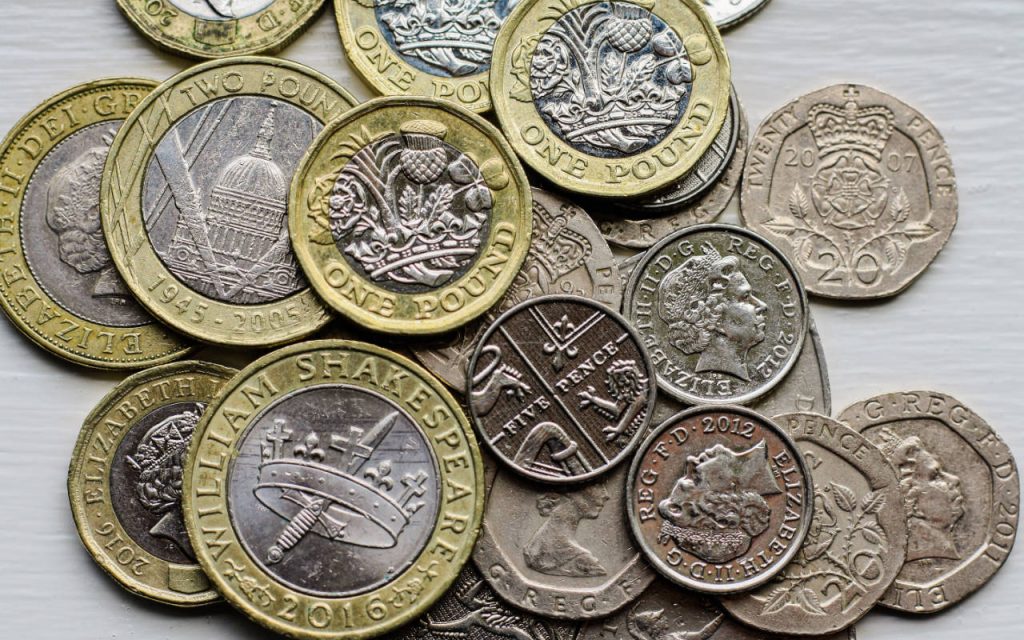English money, all coins, on a flat surface from above. There are two pound coins, one pound coins, twenty pence coins and five pence pieces in the picture.