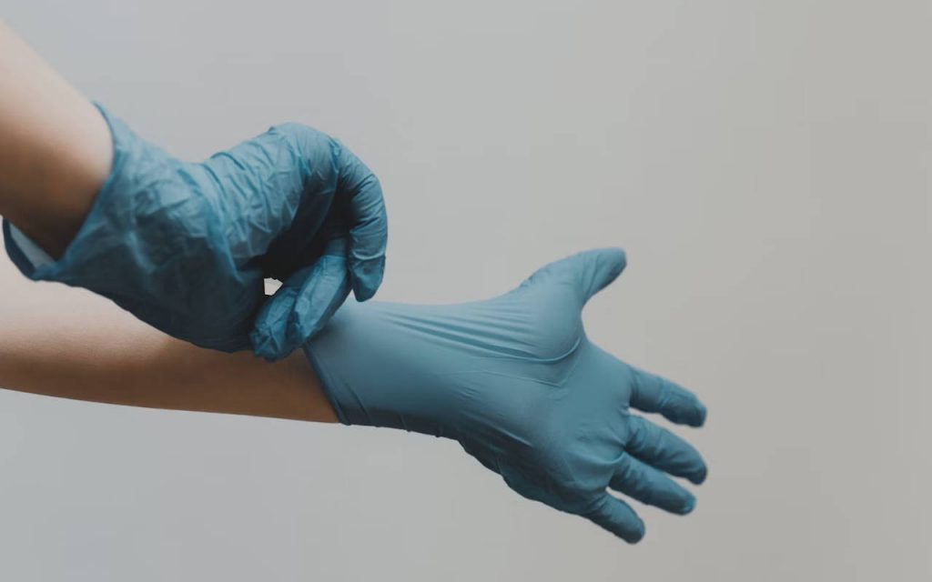 A person puts on PPE gloves on a grey background. Only arms visible, no body or face in shot.