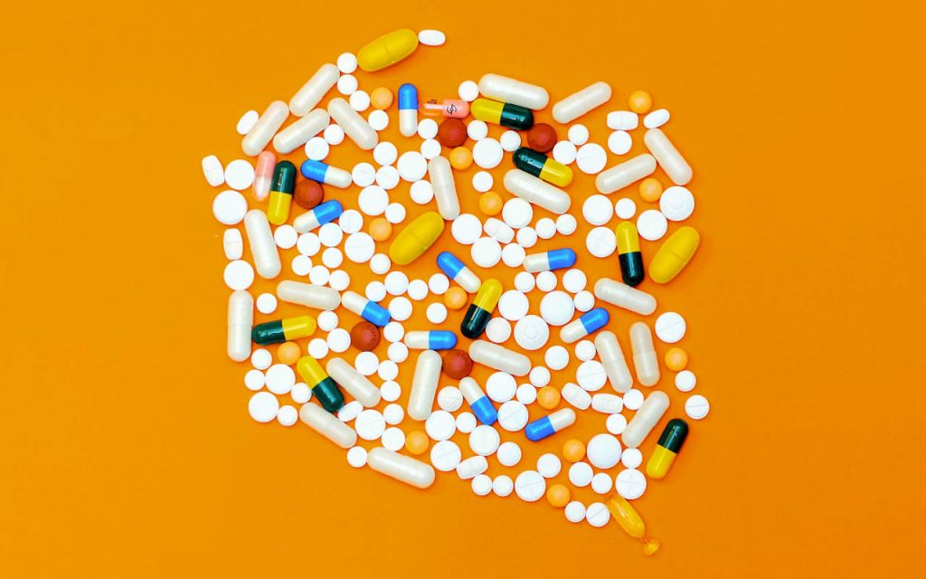 Flat lay photo of unpackaged medicines – various pills on an orange background.
