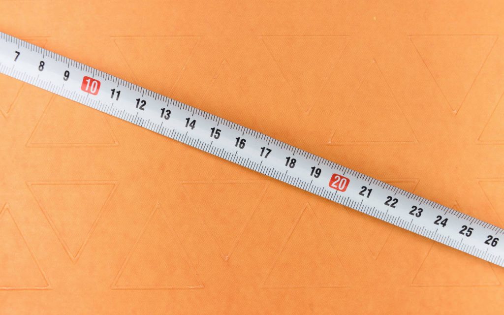 Image of a tape measure, for measuring large polythene bags, photographed against a textured orange background.