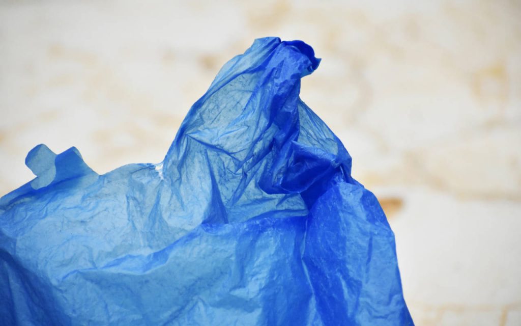 Closeup photo of a blue polythene bag. Background is blurred out heavily, but appears to be a beach on a cloudy day or a quarry.